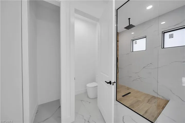 Walk-in shower with full-height glass enclosure, wood-finish flooring, and two transom windows