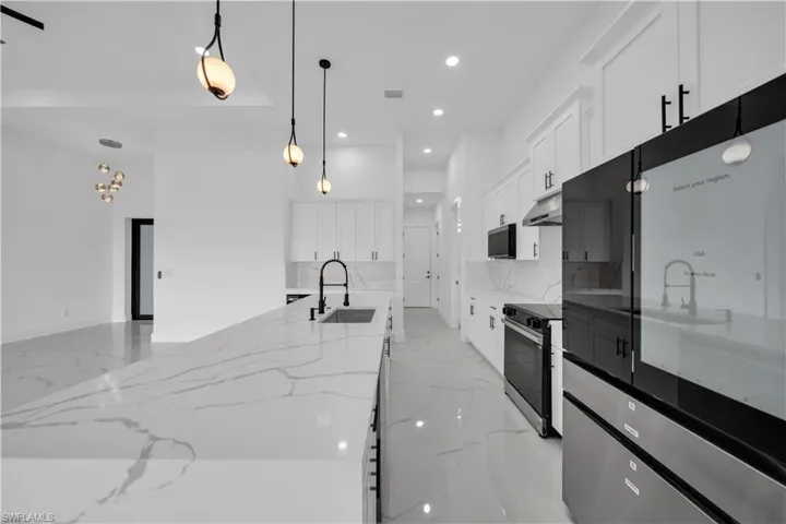 Spacious kitchen featuring a large island with a sink, white cabinetry, a built-in range with an overhead microwave, and a modern refrigerator