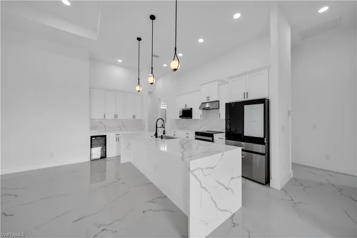 Kitchen featuring a waterfall island with integrated sink, white cabinetry, integrated stainless steel appliances, and large format tile flooring