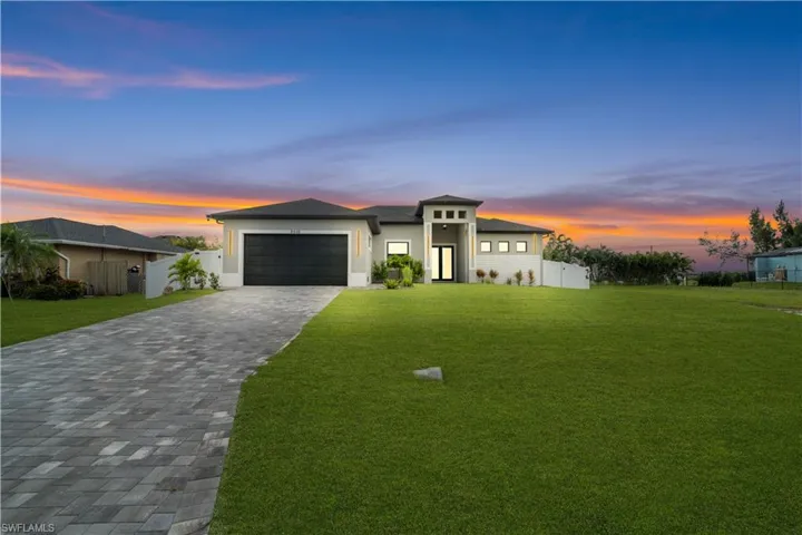 Contemporary stucco exterior with a prominent entry tower, black garage door, paver driveway, and a spacious front lawn