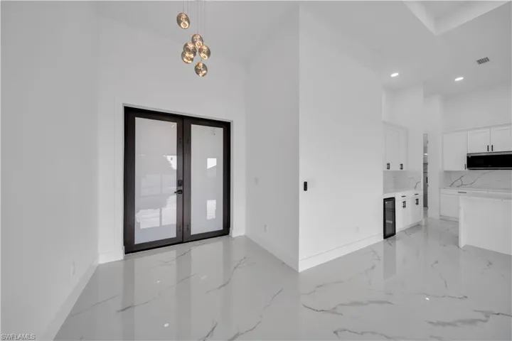 Double entry doors, high ceilings, globe pendant lighting, white cabinetry, and large-format tile flooring