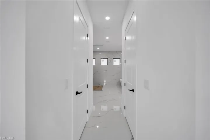Crisp white walls, recessed lighting, white paneled doors with matte black hardware, and polished tile flooring extending into the background