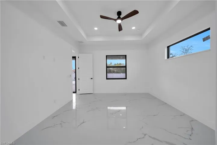 Tray ceiling with recessed lighting and a ceiling fan, white paneled door, and large format tile flooring