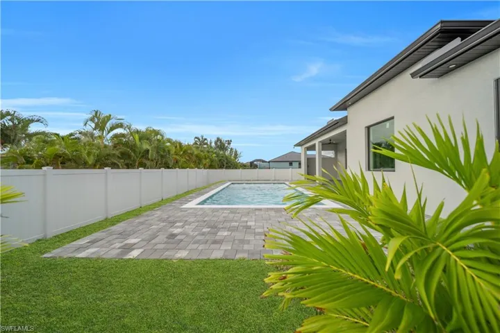 Outdoor swimming pool with paver decking, a white privacy fence, and a stucco exterior