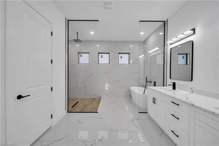 Spacious bathroom featuring a dual vanity with undermount sinks, a freestanding tub, a walk-in shower with glass enclosure, rain shower head, and floor-to-ceiling marble-look tile