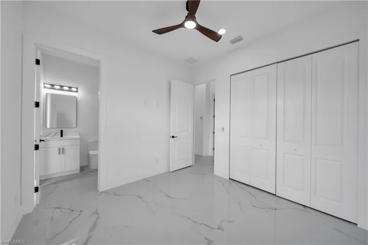 High ceilings with a ceiling fan, wide bi-fold closet doors, polished tile flooring, and an en-suite bathroom featuring a vanity with an integrated sink and wall-mounted lighting