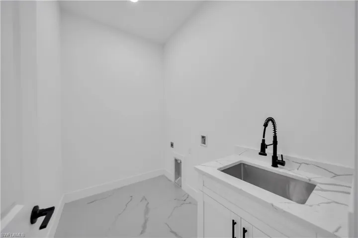 Laundry area with a utility sink, white cabinetry, a matte black gooseneck faucet, light-toned flooring, and a stone-finish countertop