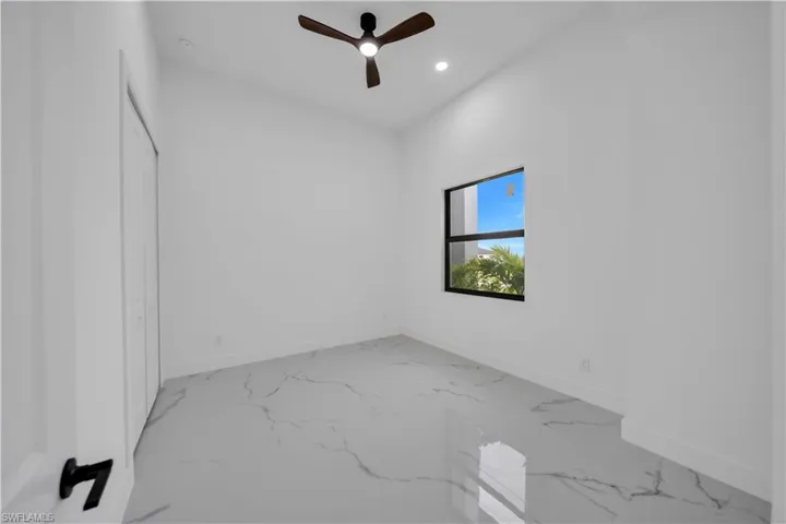 White walls, recessed lighting, and a dark wood-finish ceiling fan complement the large window with black framing