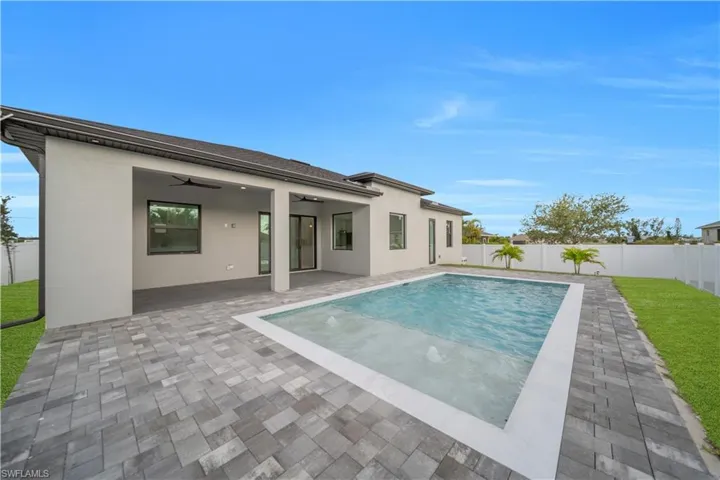 Rear exterior featuring an in-ground swimming pool, gray paver patio, covered patio, and a privacy fence