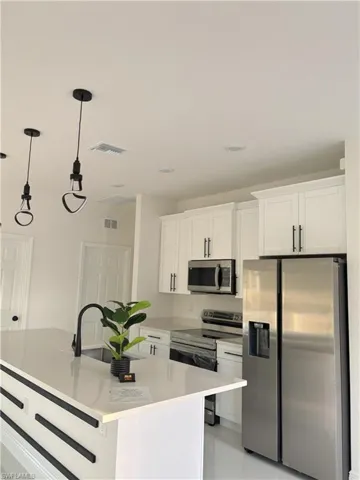 Kitchen with stainless steel appliances, a kitchen island with sink, white cabinets, hanging light fixtures, and light stone countertops