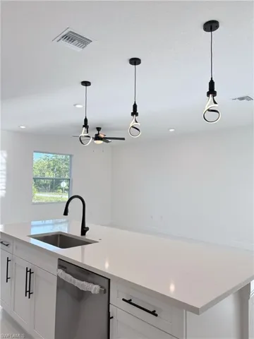 Kitchen featuring stainless steel dishwasher, light countertops, pendant lighting, white cabinets, and recessed lighting