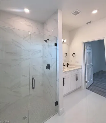 Full bathroom with a marble finish shower, vanity, and recessed lighting