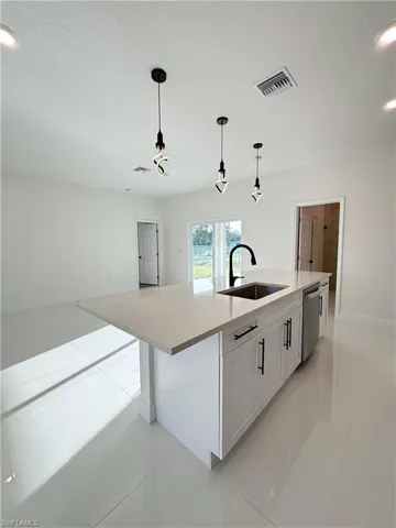 Kitchen with stainless steel dishwasher, a kitchen island with sink, light tile patterned flooring, decorative light fixtures, and light countertops