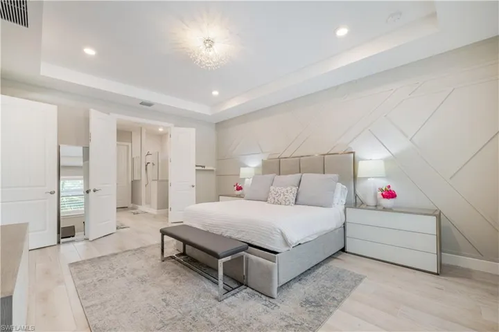 Bedroom featuring light wood finished floors, recessed lighting, a tray ceiling, and a decorative wall