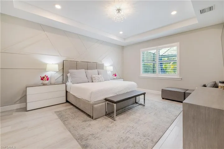 Bedroom featuring a raised ceiling, light wood finished floors, a decorative wall, recessed lighting, and a chandelier