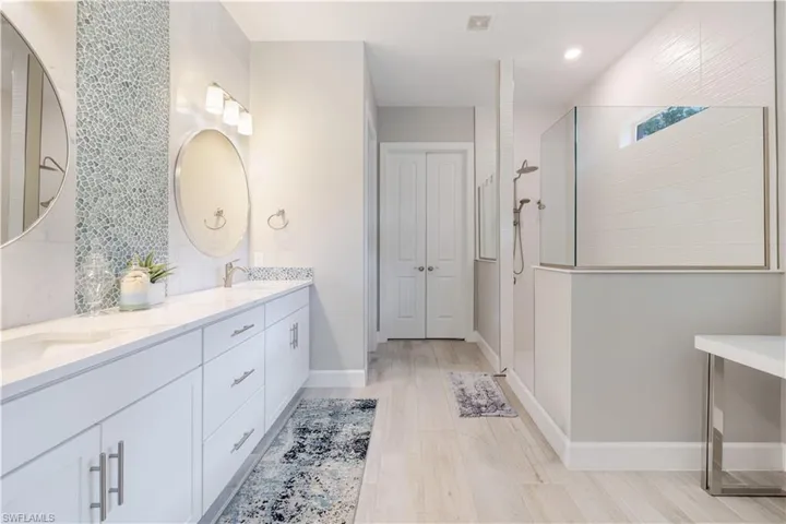 Full bathroom featuring walk in shower, double vanity, light wood-style flooring, and decorative backsplash