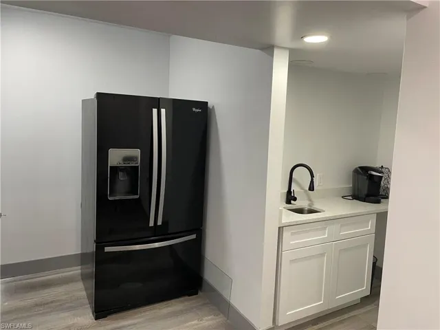 Kitchen with black fridge with ice dispenser, light stone counters, white cabinets, and light wood finished floors