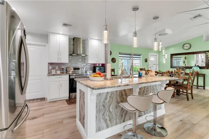 Kitchen with wall chimney range hood, light wood-type flooring, white cabinetry, and appliances with stainless steel finishes