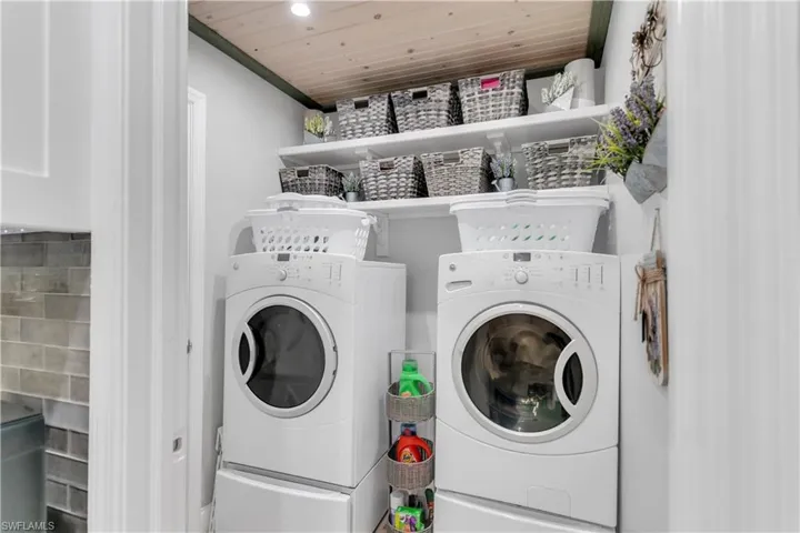 Clothes washing area with separate washer and dryer and wood ceiling