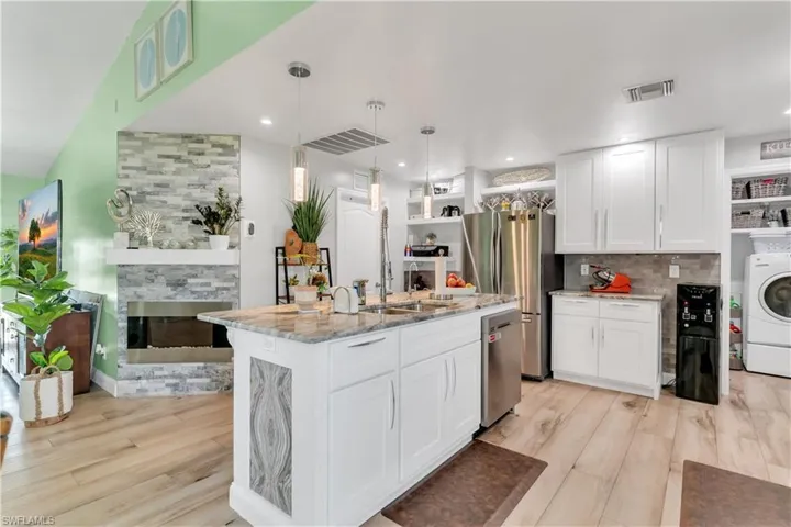 Kitchen with light hardwood / wood-style flooring, light stone countertops, an island with sink, washer / dryer, and white cabinets