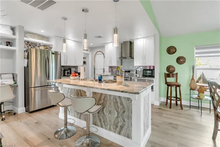 Kitchen with wall chimney range hood, light wood-type flooring, decorative backsplash, white cabinets, and stainless steel appliances