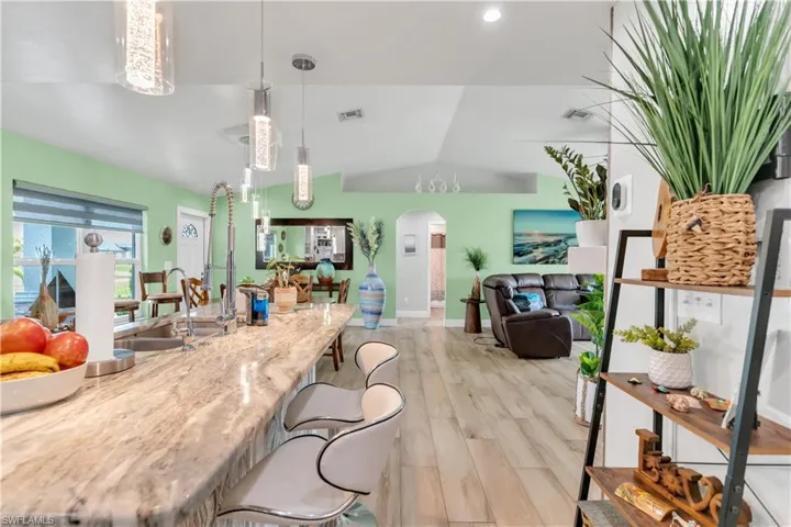 Kitchen with sink, light wood-type flooring, a breakfast bar area, vaulted ceiling, and hanging light fixtures