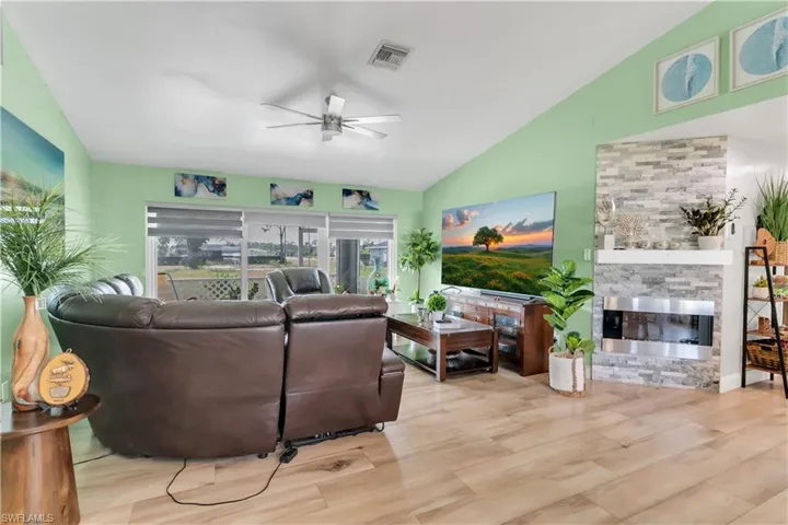 Living room featuring light hardwood / wood-style flooring, ceiling fan, a stone fireplace, and vaulted ceiling