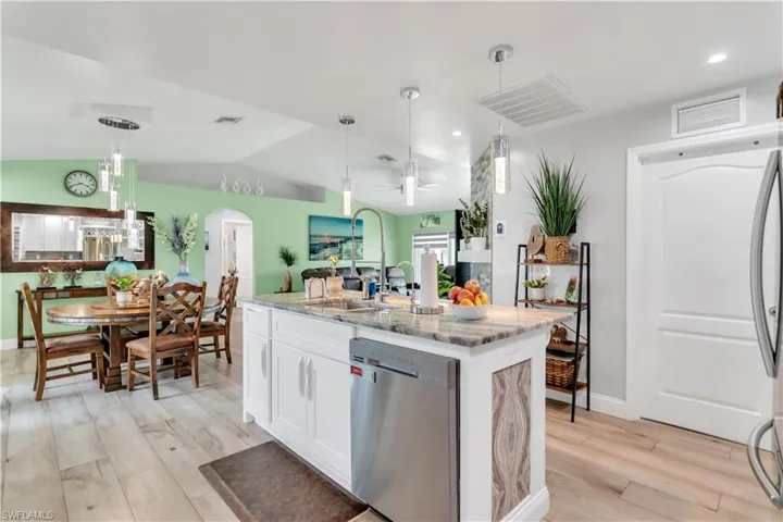 Kitchen featuring light stone countertops, light hardwood / wood-style floors, vaulted ceiling, dishwasher, and ceiling fan