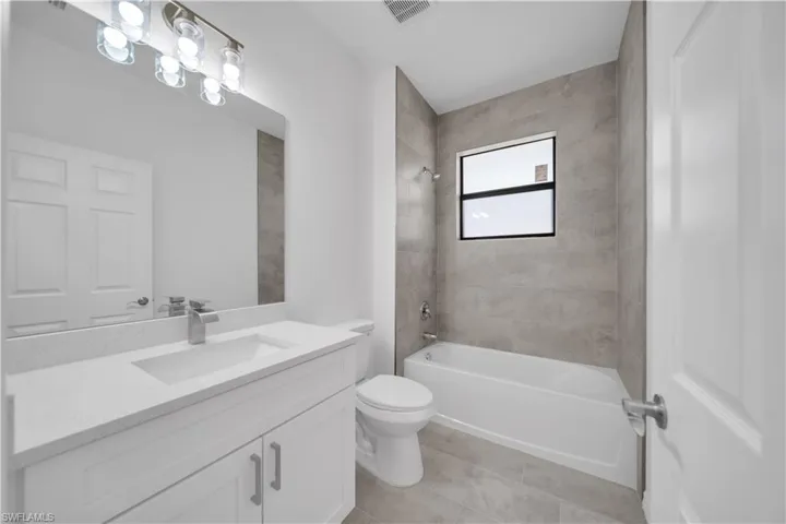 Bathroom with washtub / shower combination, vanity, and light tile patterned flooring