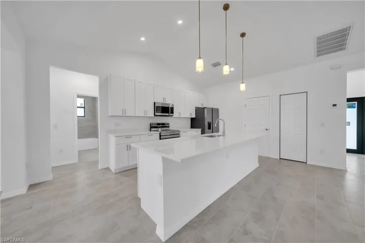Kitchen featuring white cabinets, appliances with stainless steel finishes, decorative light fixtures, a kitchen island with sink, and vaulted ceiling