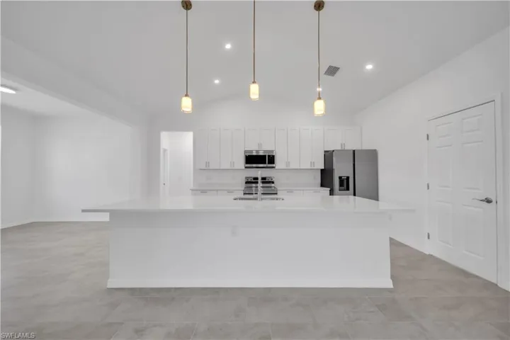Kitchen featuring lofted ceiling, stainless steel appliances, white cabinets, light stone countertops, and a kitchen island with sink