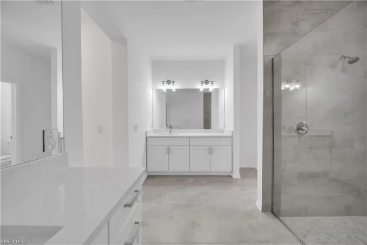 Full bathroom featuring two vanities, walk in shower, and light tile patterned flooring