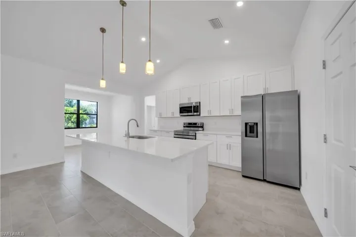 Kitchen featuring appliances with stainless steel finishes, hanging light fixtures, white cabinets, vaulted ceiling, and a kitchen island with sink