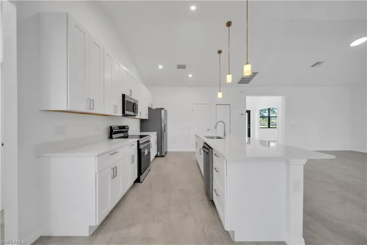 Kitchen with stainless steel appliances, decorative light fixtures, recessed lighting, white cabinets, and a center island with sink
