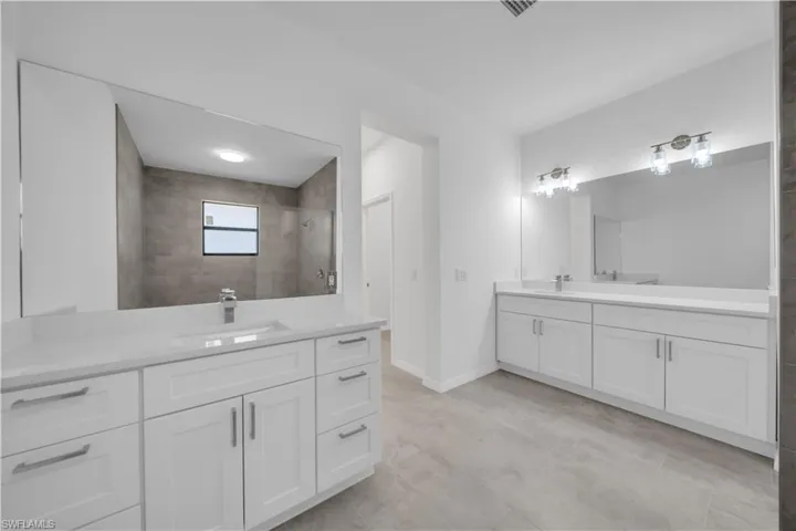 Bathroom with two vanities, tiled shower, and light tile patterned floors
