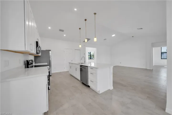 Kitchen featuring white cabinets, pendant lighting, an island with sink, light stone counters, and stainless steel appliances