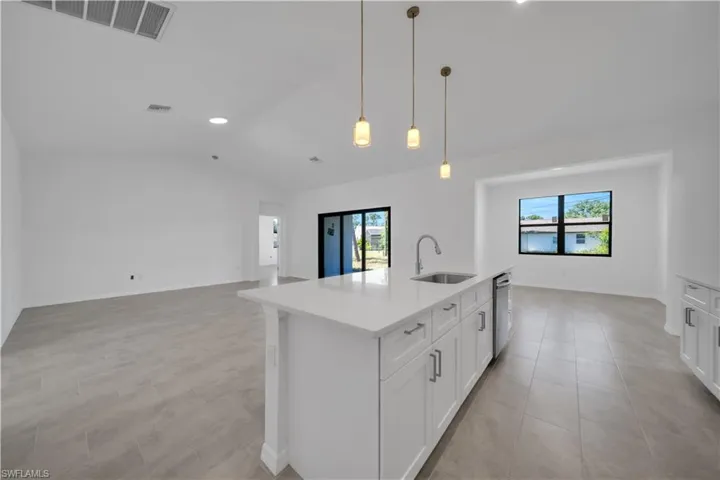 Kitchen with open floor plan, an island with sink, white cabinets, vaulted ceiling, and light stone countertops
