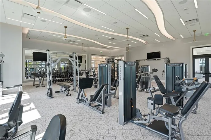 Fitness center featuring a suspended drop ceiling with integrated linear LED lighting, wall-to-wall mirror, patterned commercial-grade carpeting, and ceiling-mounted fans