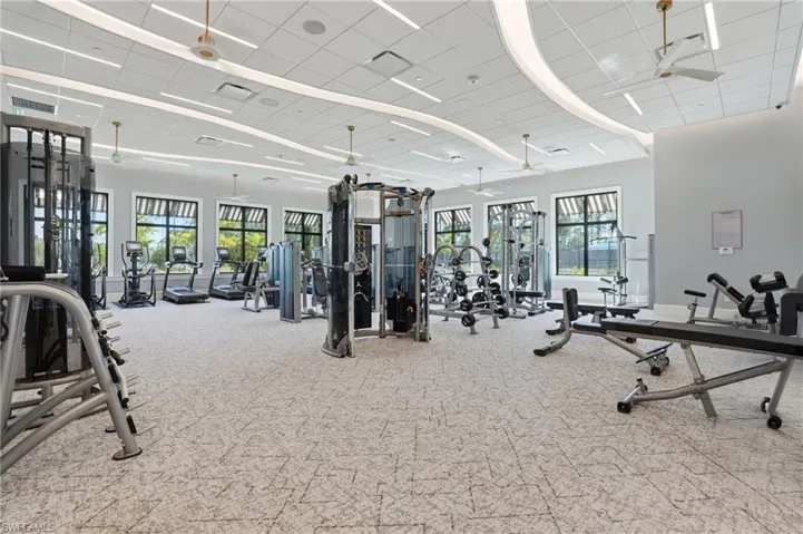 Fitness center featuring expansive floor space, recessed linear lighting, acoustic drop ceiling, multiple large windows, and patterned commercial-grade flooring