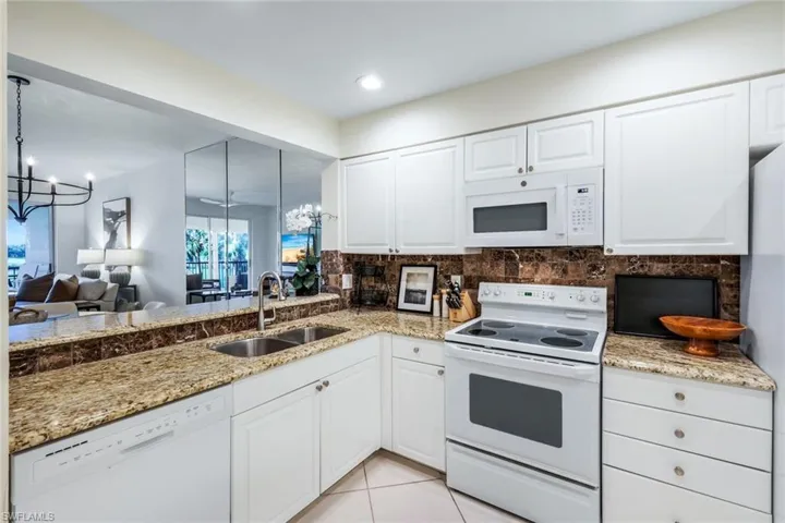 Kitchen featuring a chandelier, white appliances, white cabinets, and light stone counters