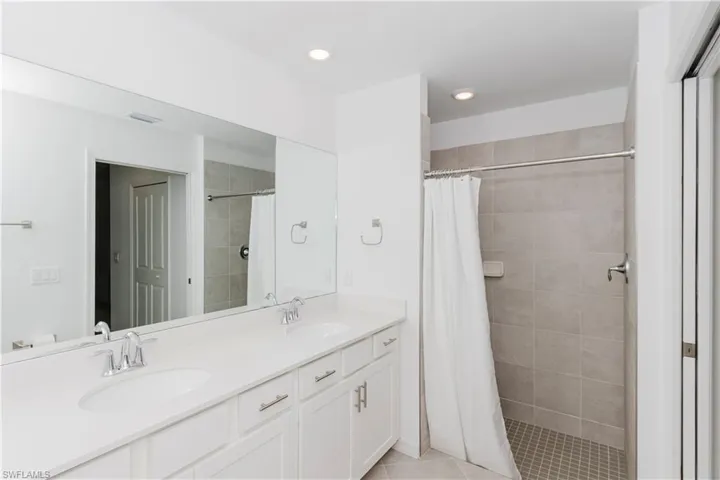 Full bath with double vanity, tiled shower, recessed lighting, and light tile patterned floors