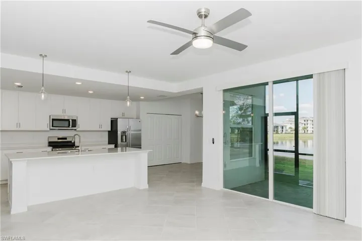 Kitchen featuring stainless steel appliances, white cabinets, a center island with sink, hanging light fixtures, and ceiling fan
