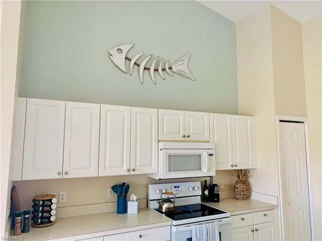 Kitchen featuring white appliances, light countertops, and white cabinetry