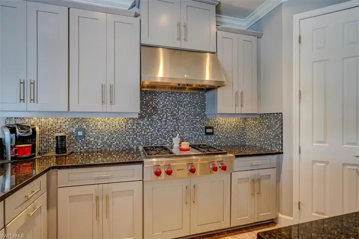 Kitchen with white cabinetry, stainless steel gas stovetop, granite counters, and exhaust hood