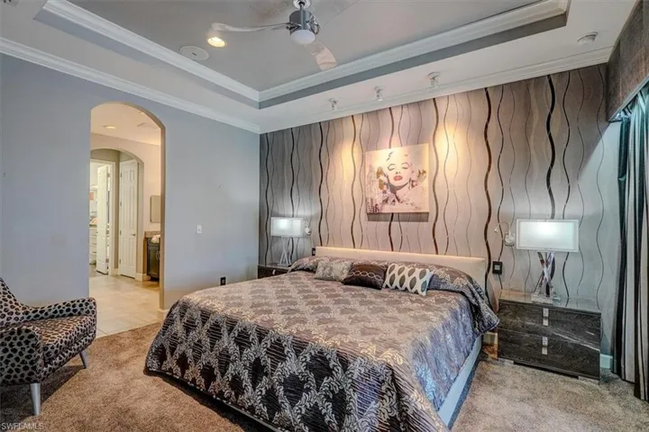 Bedroom with bathroom access and  with a tray ceiling, ornamental molding, and ceiling fan
