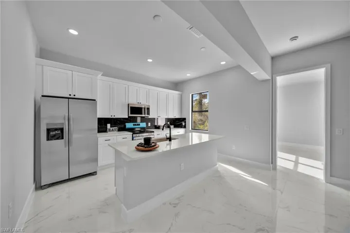 Kitchen with backsplash, stainless steel appliances, sink, white cabinetry, and an island with sink