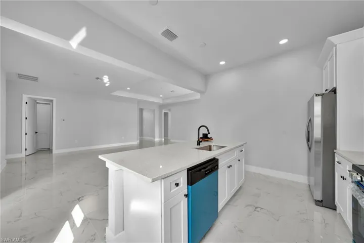 Kitchen featuring appliances with stainless steel finishes, a tray ceiling, a kitchen island with sink, sink, and white cabinetry