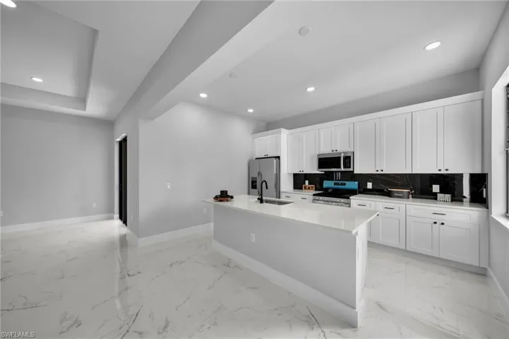 Kitchen featuring white cabinetry, sink, tasteful backsplash, an island with sink, and appliances with stainless steel finishes