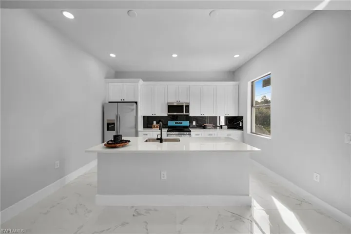 Kitchen with white cabinets, appliances with stainless steel finishes, sink, and an island with sink