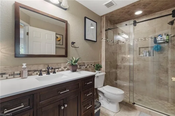 Bathroom with a textured wall, vanity, a shower stall, tile walls, and a wainscoted wall